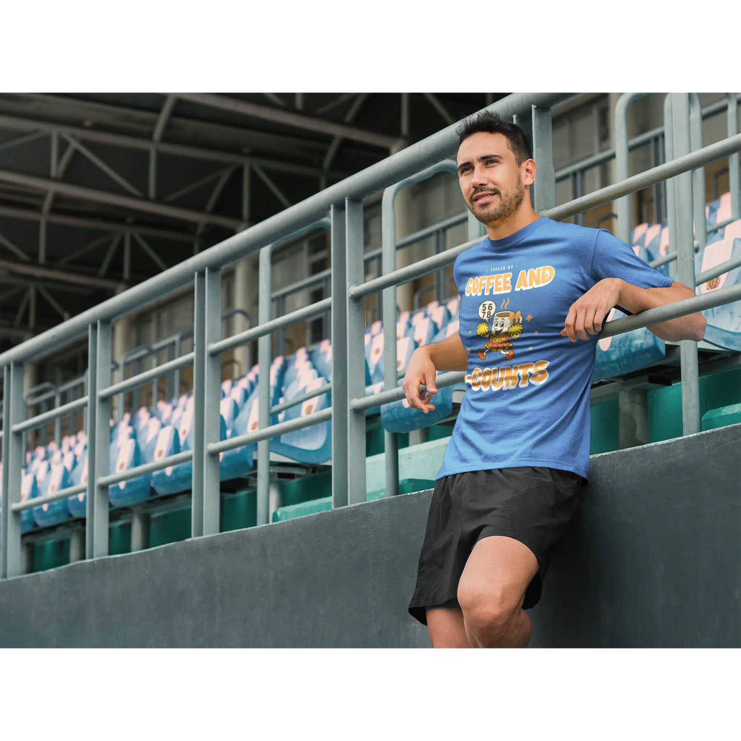 Male Cheerleading coach wearing a blue t-shirt with a cheerleading graphic design in a football stand