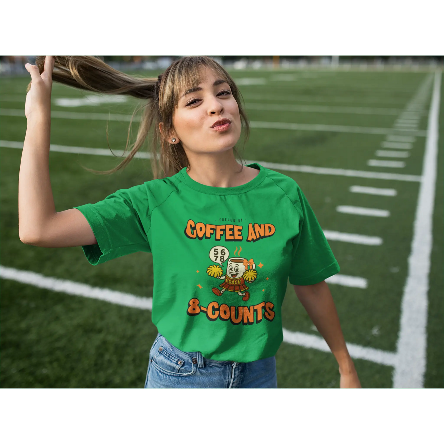 Cheerleading coach wearing a green t-shirt with a cheerleading graphic design on a football field
