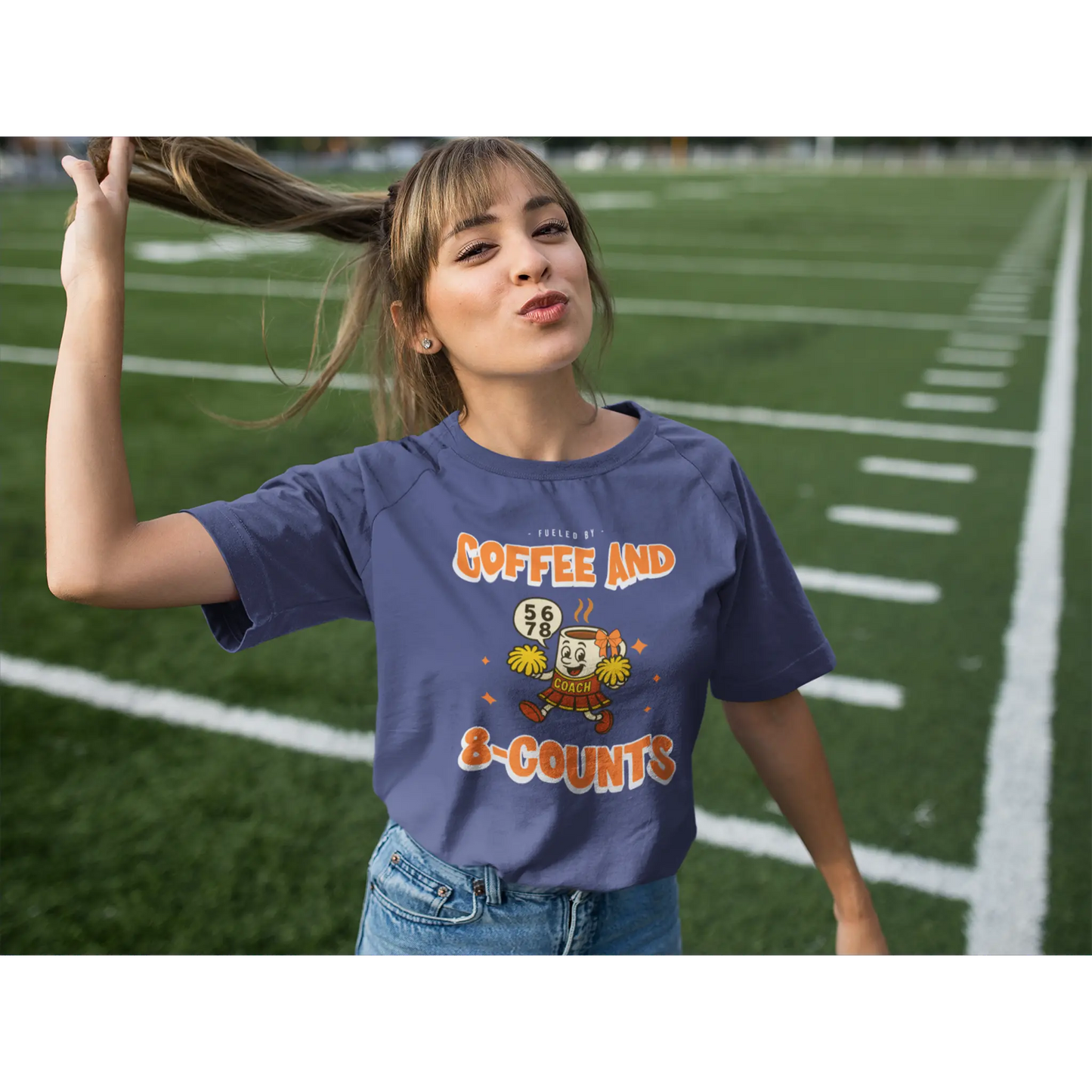 Cheerleading coach wearing a navy t-shirt with a cheerleading graphic design on a football field