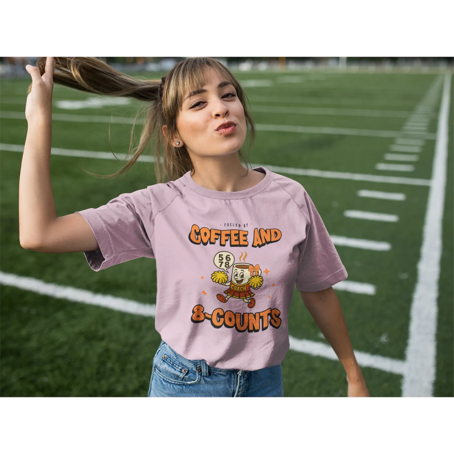 Cheerleading coach wearing a pink t-shirt with a cheerleading graphic design on a football field