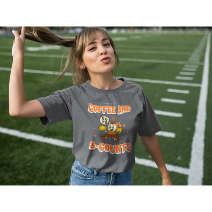 Cheerleading coach wearing a grey t-shirt with a cheerleading graphic design on a football field