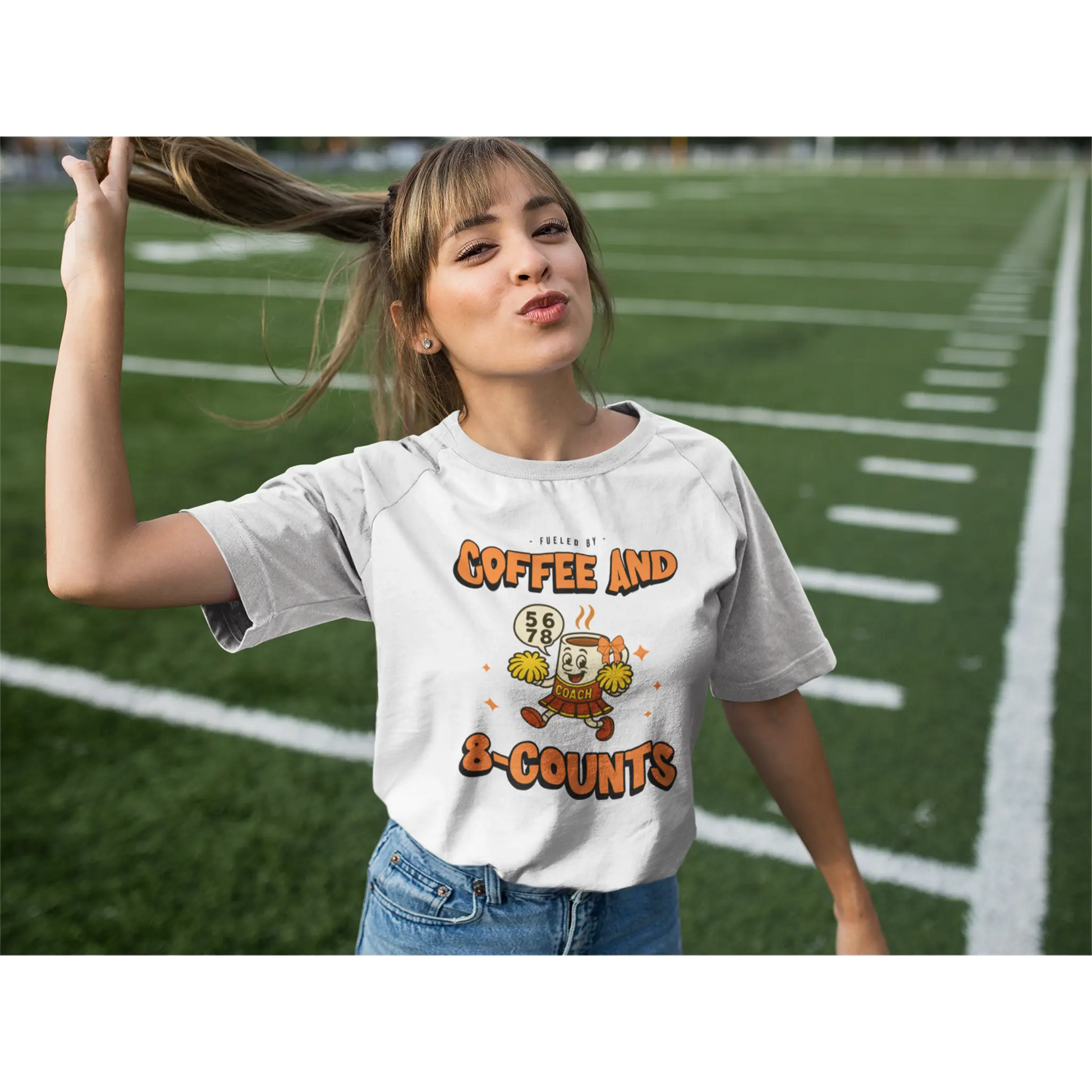 Cheerleading coach wearing a white t-shirt with a cheerleading graphic design on a football field